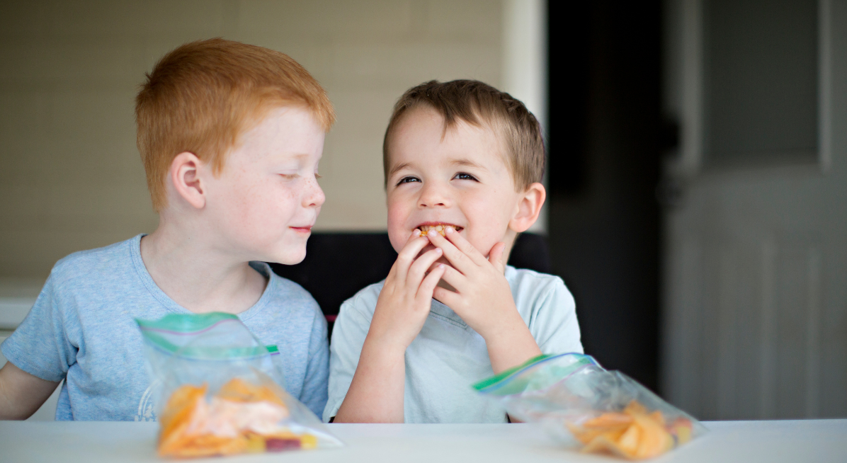 two boy toddlers eating snacks and laughing 
