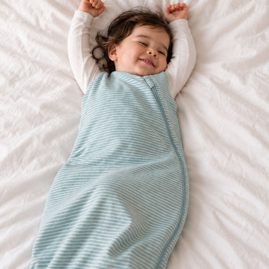A baby lying on a white bed, wrapped in a light blue and white striped zippered swaddle blanket.