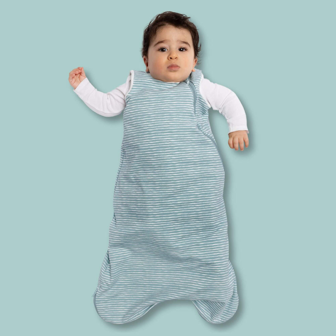 A baby lying comfortably in the Norani Baby One & Done Sleep Sack in a soft green striped pattern, designed with organic cotton and a removable 1.5 TOG insert for all-season use.