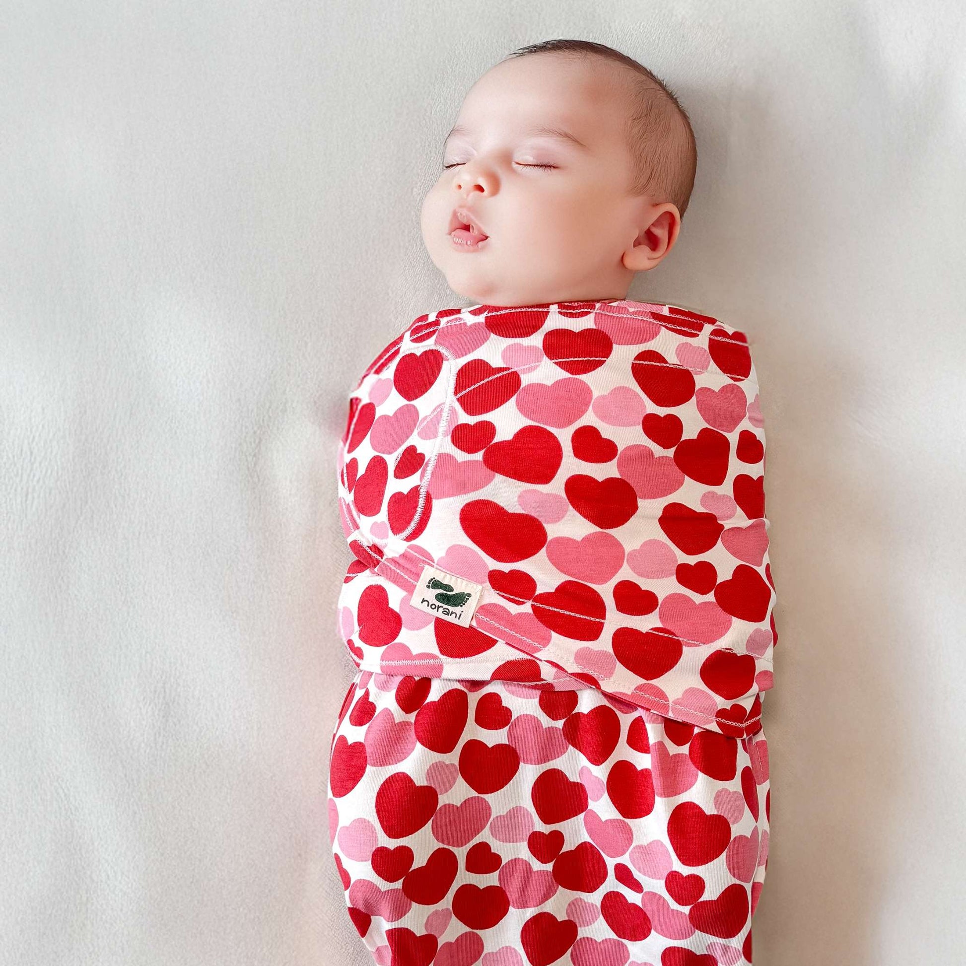 Baby swaddled in a pink and red heart-patterned blanket on a white background