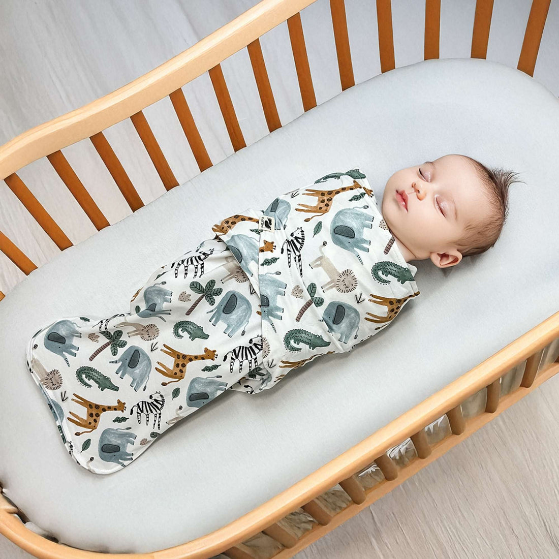 Baby sleeping in a crib with a swaddle featuring animal prints.