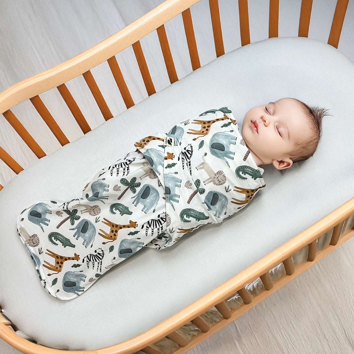 Baby sleeping in a crib with a swaddle featuring animal prints.