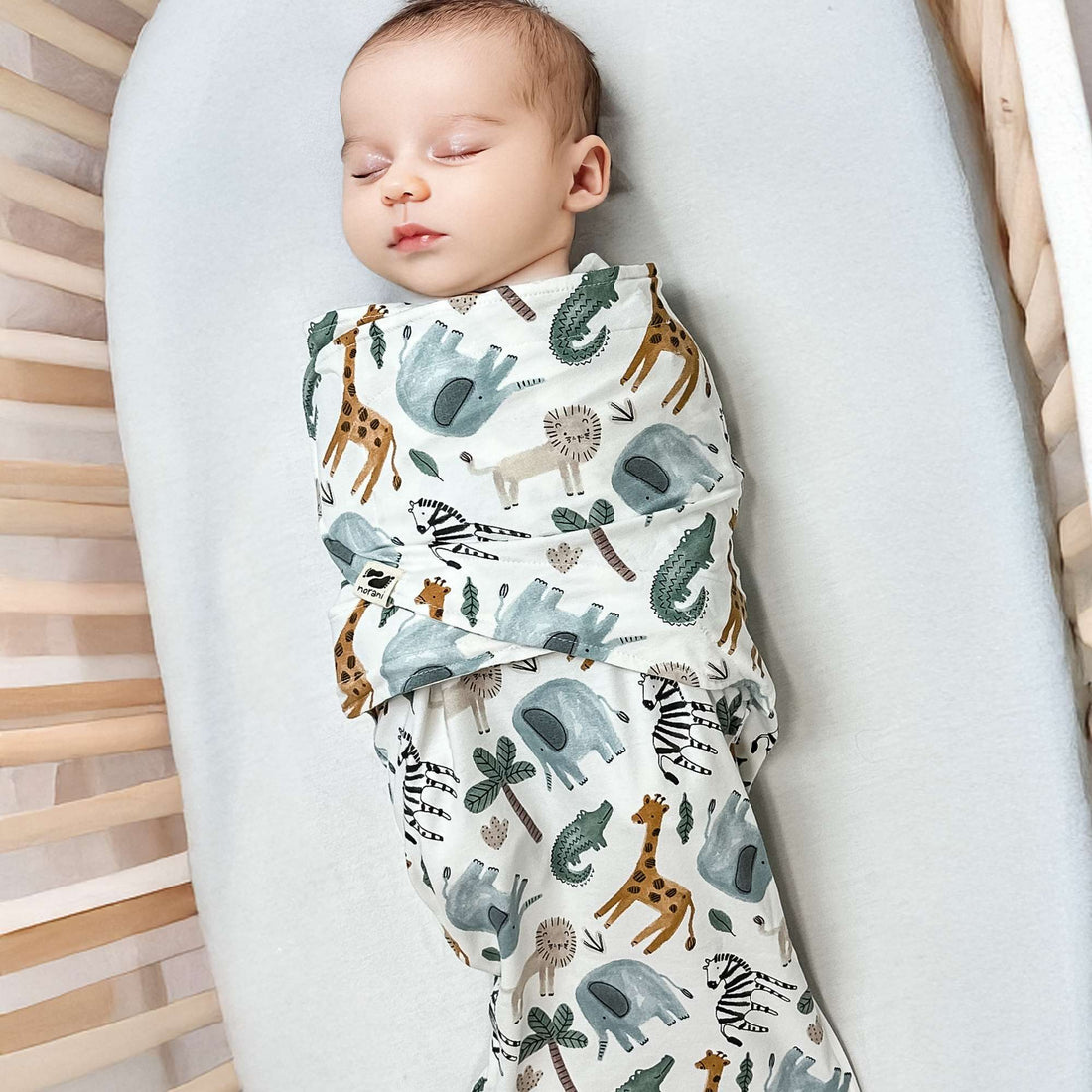 Baby swaddled in a blanket with animal patterns on a white surface
