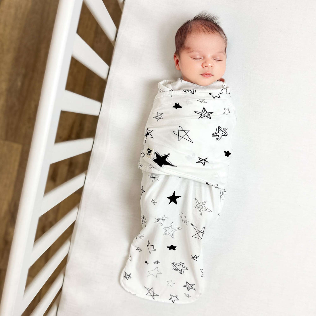 Newborn baby swaddled in a white blanket with black star patterns, lying on a white surface.