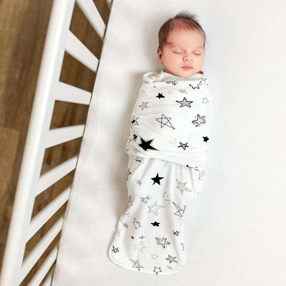 Newborn baby swaddled in a white blanket with black star patterns, lying on a white surface.