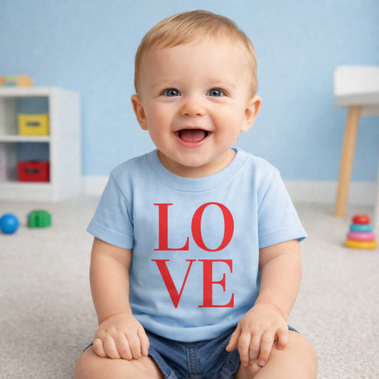 Child wearing a light blue shirt with 'LOVE' printed in red, sitting in a room with toys and a shelf.