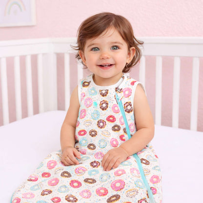 Smiling baby sitting in a crib wearing the Norani Baby One & Done Sleep Sack, made from soft GOTS-certified organic cotton with a cozy all-season design and secure zip closure.