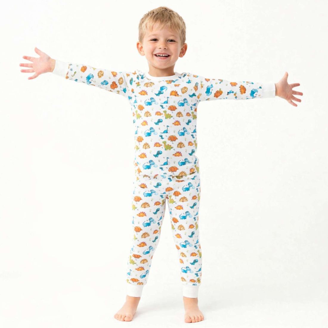 Smiling child wearing Norani Baby dinosaur print pajamas, featuring a soft organic cotton fabric and a playful dino pattern, in a bright, cozy setting.