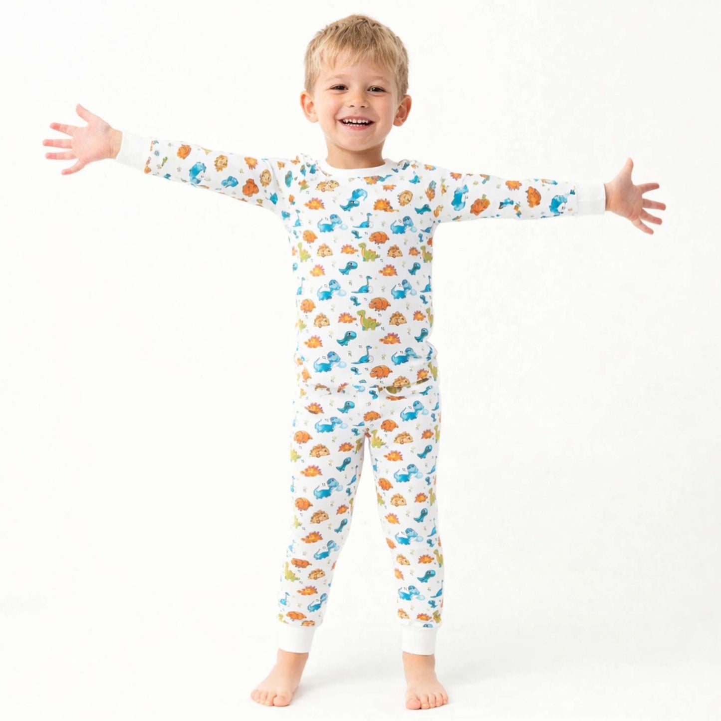 Smiling child wearing Norani Baby dinosaur print pajamas, featuring a soft organic cotton fabric and a playful dino pattern, in a bright, cozy setting.