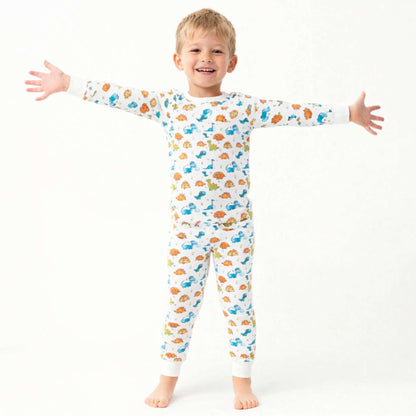 Smiling child wearing Norani Baby dinosaur print pajamas, featuring a soft organic cotton fabric and a playful dino pattern, in a bright, cozy setting.