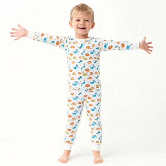 Smiling child wearing Norani Baby dinosaur print pajamas, featuring a soft organic cotton fabric and a playful dino pattern, in a bright, cozy setting.