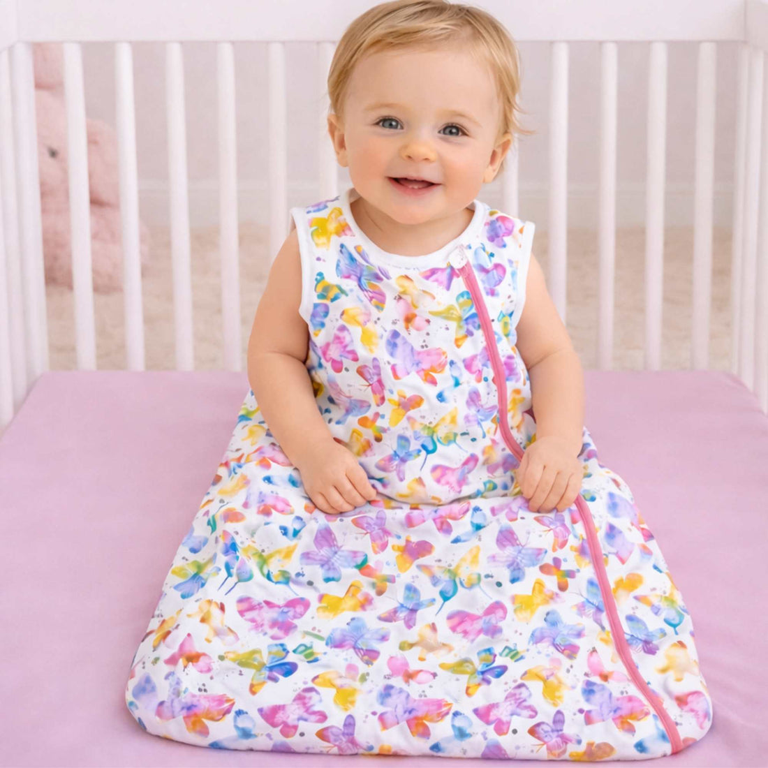 Baby sitting in a crib wearing a colorful butterfly-patterned sleep sack by norani baby