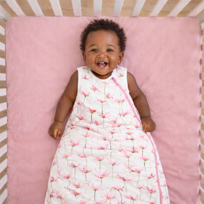 Baby lying on a pink mattress in a crib wearing the norani baby one & done sleep sack in pink petals