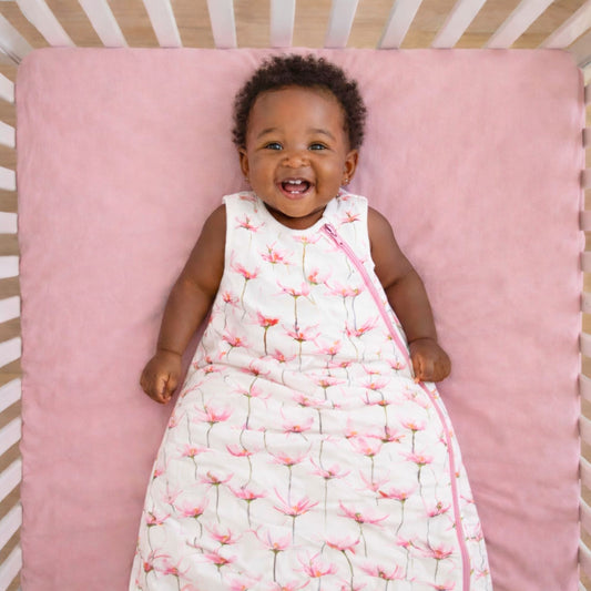 Baby lying on a pink mattress in a crib wearing the norani baby one & done sleep sack in pink petals