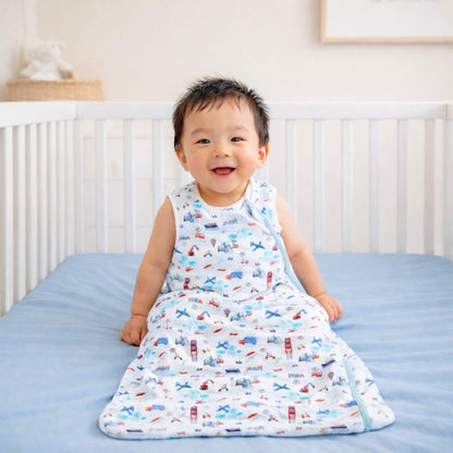 Child wearing a transportation print sleep sack by norani baby called one and done sleep sack sitting in a crib.