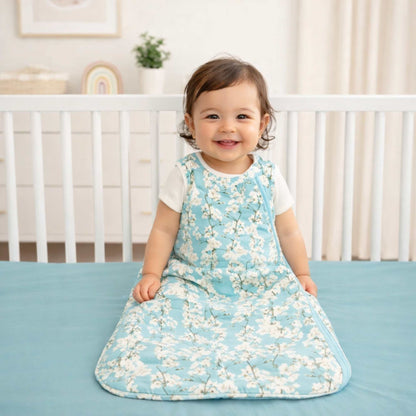Child wearing a cherry blossom sleep sack by norani baby sitting on a crib in a nursery smiling. 