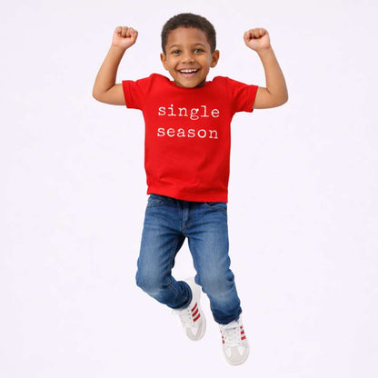 Kid mid-jump wearing a bright red T-shirt with the words “Single Season,” smiling with playful energy against a clean, minimal background.