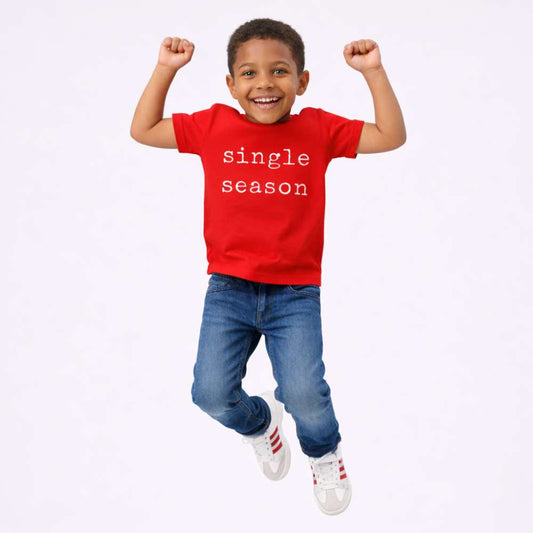 Kid mid-jump wearing a bright red T-shirt with the words “Single Season,” smiling with playful energy against a clean, minimal background.