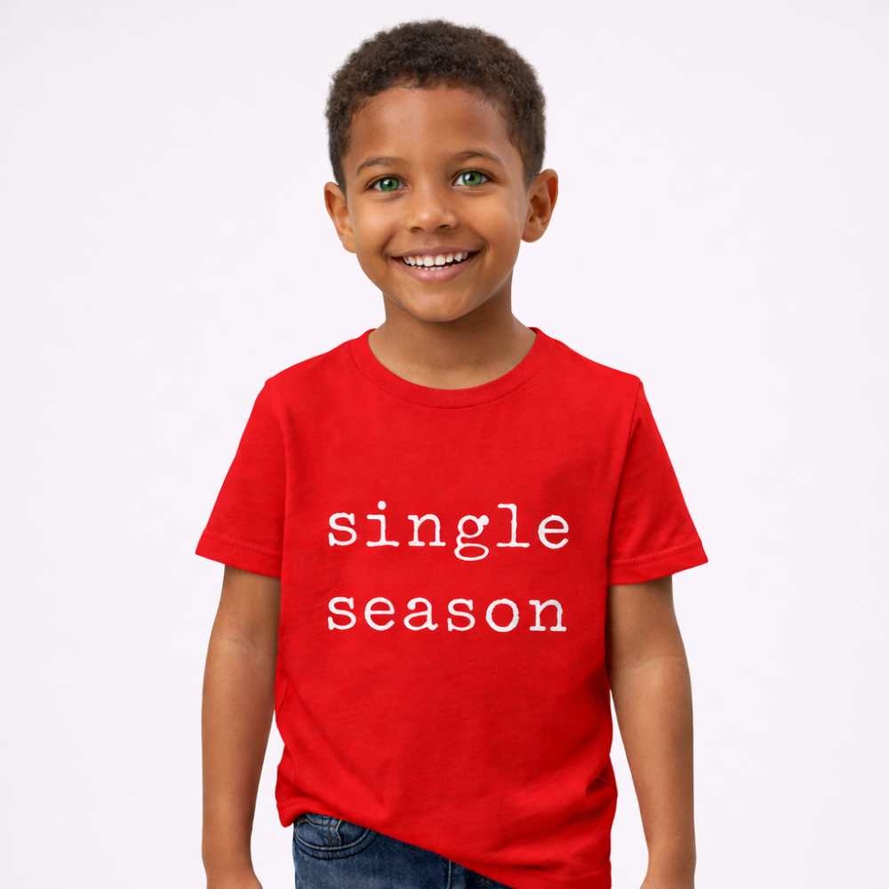Kid wearing a bright red T-shirt with the words “Single Season,” smiling with playful energy against a clean, minimal background.