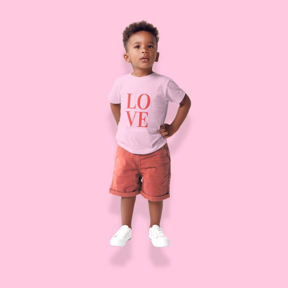 Child wearing a 'LOVE' t-shirt and red shorts on a pink background
