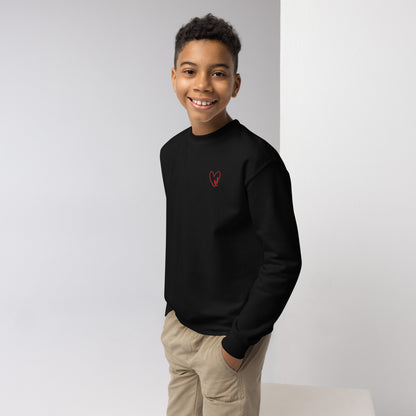 Boy smiling confidently with hands in his pockets, wearing a cozy crewneck sweatshirt featuring a small embroidered heart on the chest, styled for a casual, everyday look.